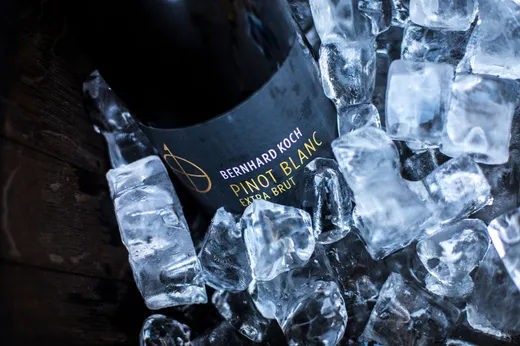 Eine Flasche Bernhard Koch Pinot Blanc Extra Brut liegt auf der Seite, umgeben von Eiswürfeln.