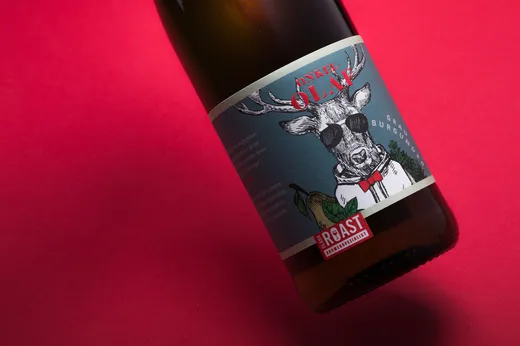 Eine Weinflasche mit einem blauen Etikett, auf dem ein Reh mit Augenklappe und Fliege vor rotem Hintergrund abgebildet ist. Auf dem Etikett stehen die Aufschriften „Blank Roast“ und „Onkel Olaf“, ergänzt durch eine grüne Blattverzierung.