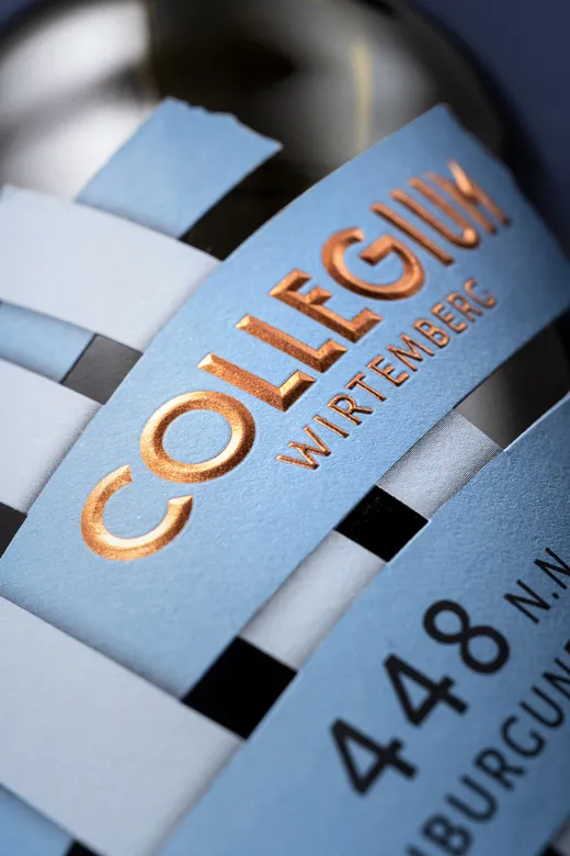 Nahaufnahme eines Flaschenetiketts mit der Aufschrift „COLLEGIUM WIRTEMBERG“ in glänzenden Goldbuchstaben und der Zahl „448“ in fetter schwarzer Schrift auf einem stilvollen blau-weißen Hintergrund.