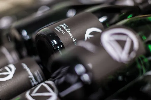 Nahaufnahme mehrerer seitlich liegender Weinflaschen mit dunklen Etiketten, auf denen weißer Text und abstrakte Motive zu sehen sind. Der Fokus liegt auf dem Etikett mit der Aufschrift „Finkenauer Riesling trocken“, während andere Flaschen im Vordergrund unscharf erscheinen.