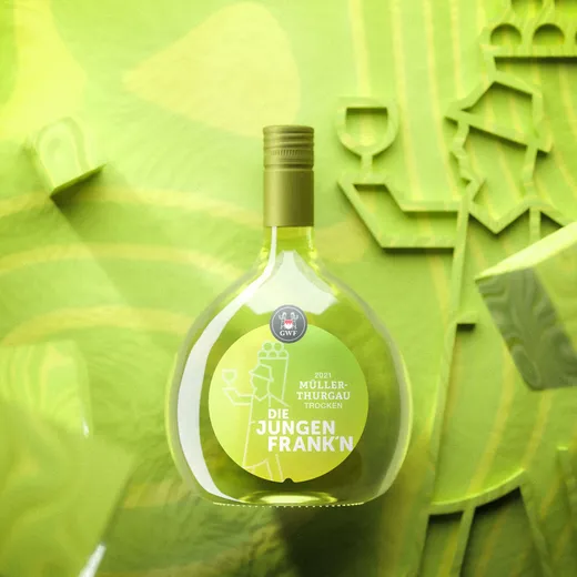 Eine grüne Weinflasche mit der Aufschrift „2021 Müller-Thurgau Trocken Die Jungen Frank’n“ steht aufrecht vor einem leuchtenden, abstrakten grünen Hintergrund mit stilisierten Motiven rund um das Thema Wein.