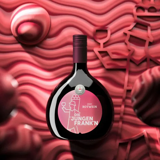 Eine runde, dunkle Weinflasche mit einem rosa Etikett, auf dem „2021 Rotwein Die Jungen Frank’n“ steht, ist vor einem wellenförmigen, rosa-roten, abstrakten Hintergrund platziert, der mit Strichzeichnungen zum Thema Wein verziert ist.