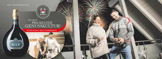 Ein Paar steht auf einem Balkon, trinkt Wein und genießt nachts ein Feuerwerk. Zu sehen sind eine Flasche „Cult“-Sekt und ein rundes Etikett mit Text. Einblendung: Eine Gruppe trinkt drinnen Wein. Die Szene vermittelt ein Gefühl von Feierlichkeit und Genuss.