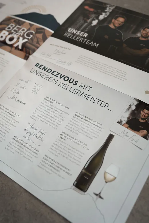 Eine Seite aus einer deutschsprachigen Zeitschrift oder Broschüre zeigt Inhalte zum Thema Wein, darunter Fotos von zwei Männern, einer Weinflasche, einem Glas Weißwein, handschriftlichen Unterschriften und einem stilisierten Text über ein Treffen mit dem Kellermeister.