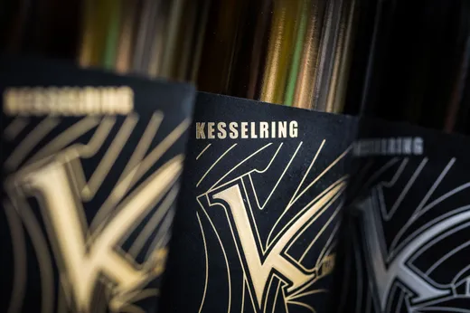 Nahaufnahme von dunklen Flaschen mit schwarz-goldenen Etiketten, auf denen der Schriftzug „KESSELRING“ und ein stilisierter Buchstabe „K“ in markanten, dekorativen Linien zu sehen sind.
