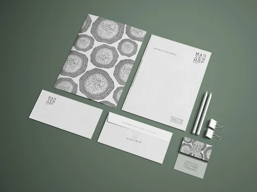 Ein Briefpapier-Set mit Markenlogo auf grünem Untergrund, bestehend aus einer Mappe mit abstrakten kreisförmigen Mustern, Briefpapier, einem Umschlag, einer Visitenkarte, zwei Bleistiften und zwei weißen Heftklammern, alles im minimalistischen, modernen Design.