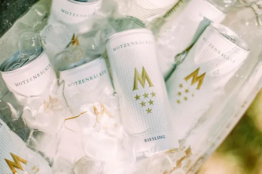 Mehrere Dosen Motzenbäcker-Riesling liegen gekühlt in einem Eisbett, an den Dosen ist Kondenswasser zu sehen. Die Dosen sind weiß und mit goldenen Akzenten und Schriftzügen versehen.