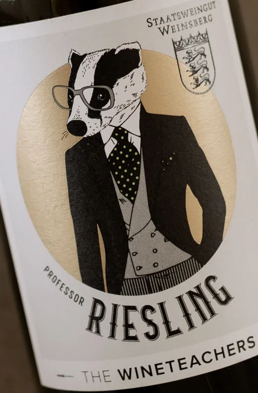 Ein Weinetikett mit der Abbildung eines Dachses in Anzug, Krawatte und Brille, auf dem „Professor Riesling“ steht, darunter „The Wineteachers“ und oben rechts ein Wappen mit deutschem Text.