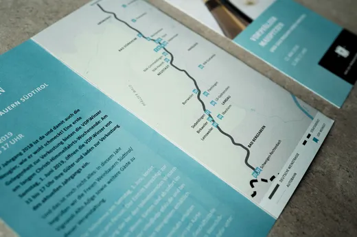 Eine Nahaufnahme einer Broschüre mit einer Karte, auf der eine Route durch Ortschaften in Südtirol, Italien, eingezeichnet ist. Die Broschüre enthält deutschen Text und Symbole, die Sehenswürdigkeiten entlang der Route kennzeichnen.